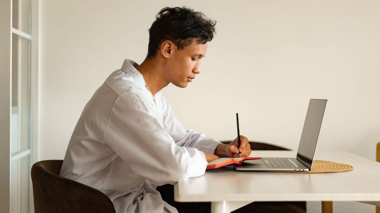 A student working through study notes at a desk beside a laptop