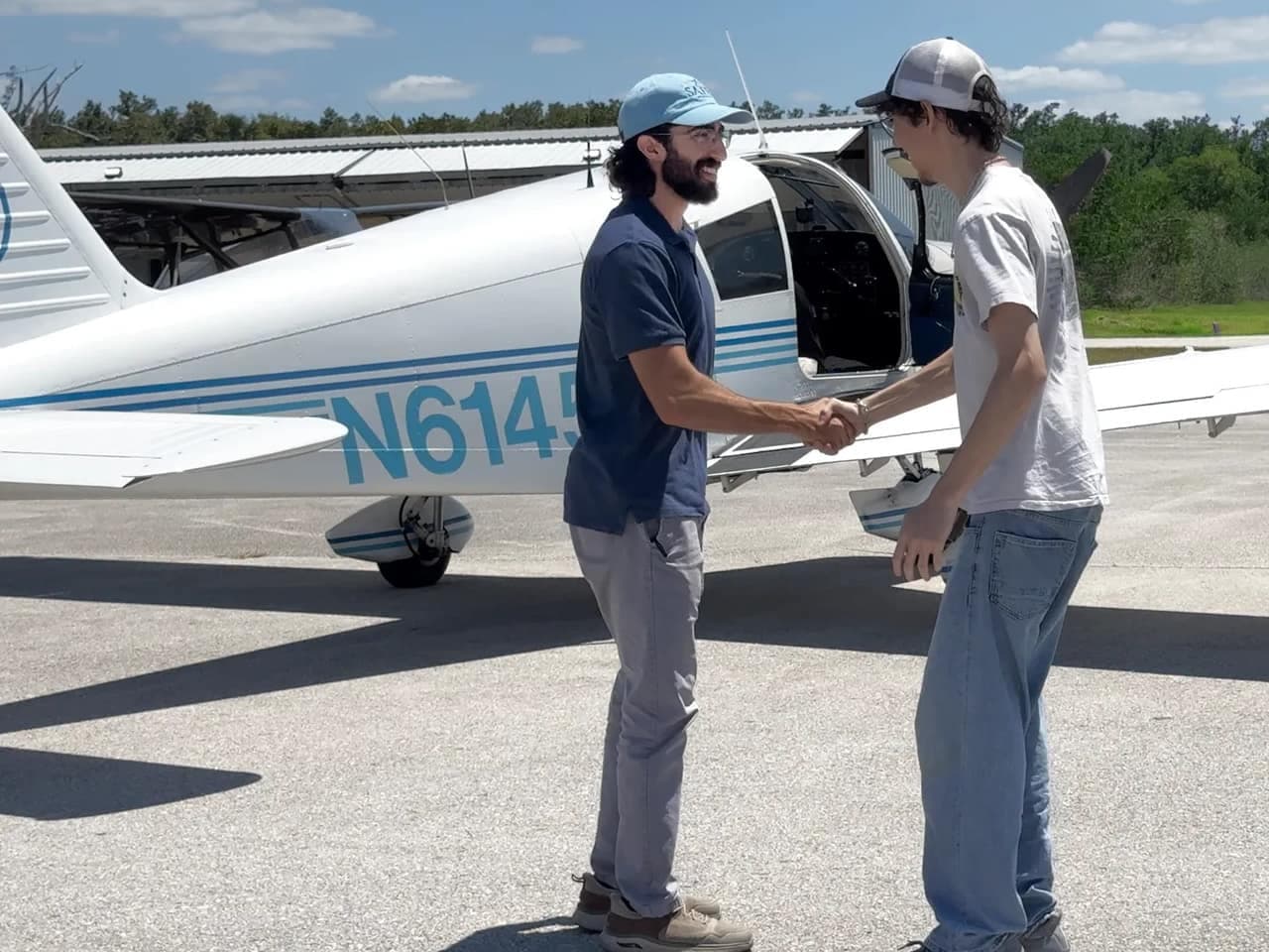 The flight instructor shaking hands with a student pilot beside the Cherokee 140 on the ramp